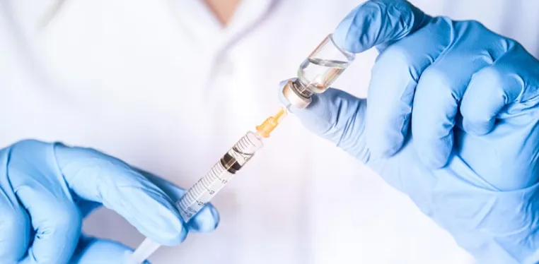 A closeup photo of a doctor's hands wearing blue latex gloves as he pulls medicine from a small bottle with a syringe