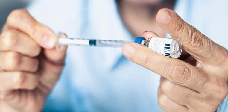 A closeup photo of a doctor's hands as he pulls medicine from a small bottle with a syringe