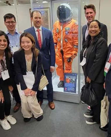 A group of Academy members pose in front of a NASA space suit