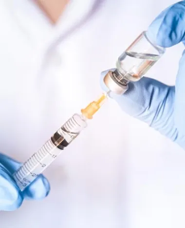 A closeup photo of a doctor's hands wearing blue latex gloves as he pulls medicine from a small bottle with a syringe