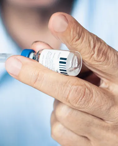 A closeup photo of a doctor's hands as he pulls medicine from a small bottle with a syringe
