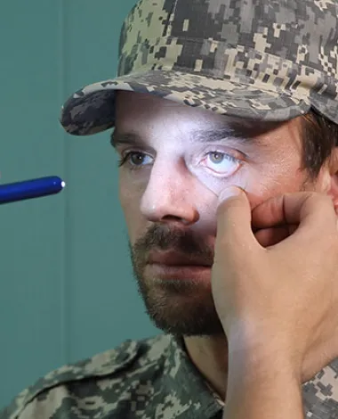 A doctor examines the eyes of a man wearing fatigues by shining a light into his pupils