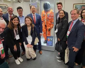A group of Academy members pose in front of a NASA space suit