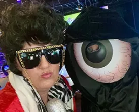 A person dressed in a Halloween costume poses next to an inflatable eyeball