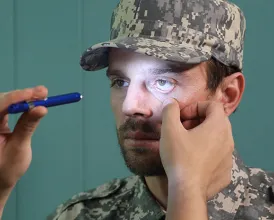 A doctor examines the eyes of a man wearing fatigues by shining a light into his pupils
